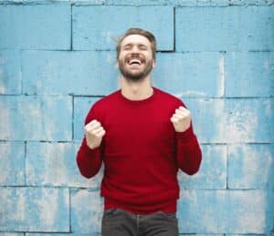 A man in red sweater in front of a wall looks so happy.
