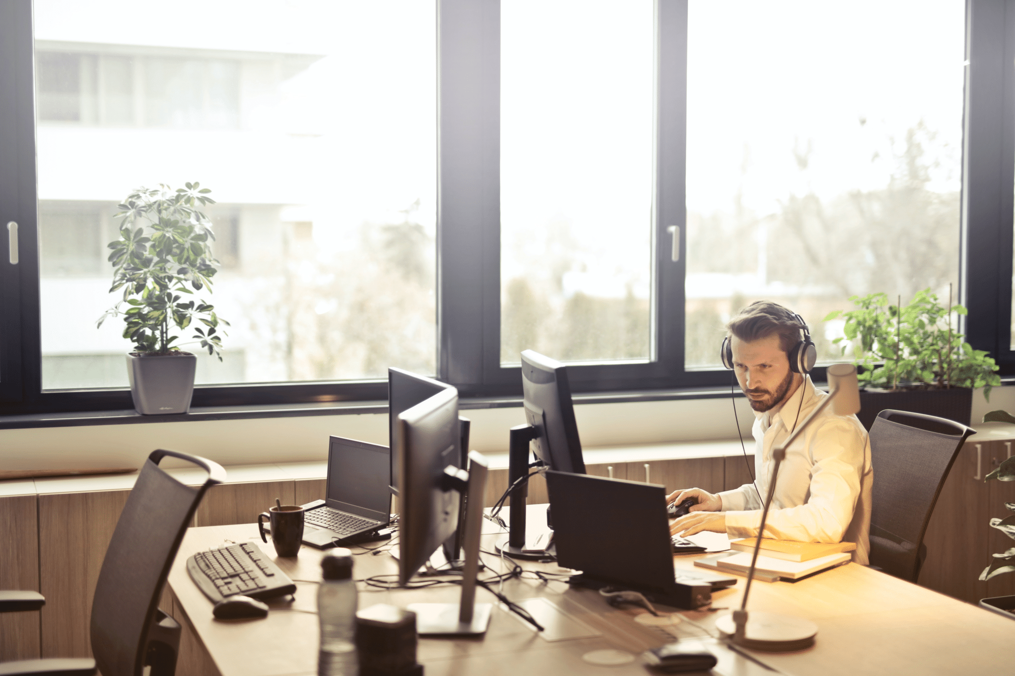 A customer service representative wearing a headset, working at a desk with multiple monitors in a bright office space.